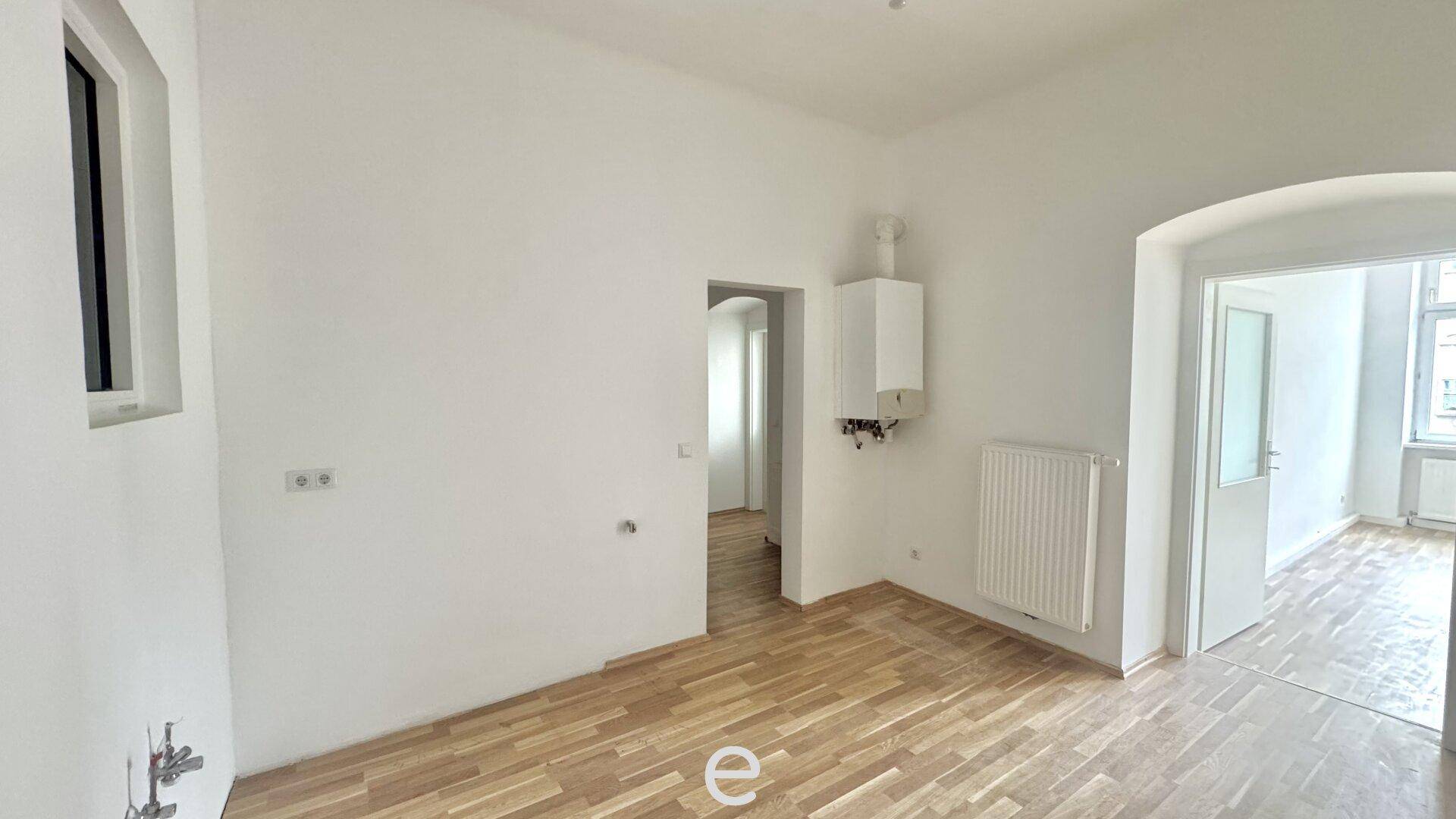 Leerer Küchenbereich mit Gastherme, Heizkörper und Holzboden, bereit für die Einrichtung.