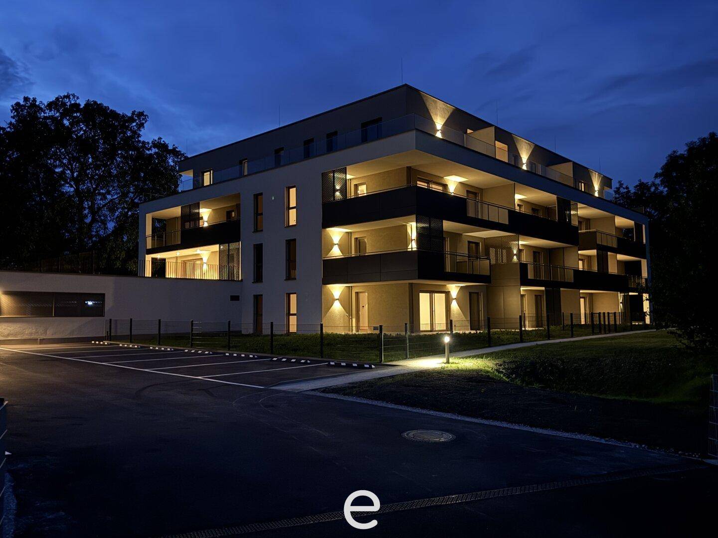 Moderne Wohnanlage bei Nacht mit beleuchteter Fassade und Außenparkplätzen.