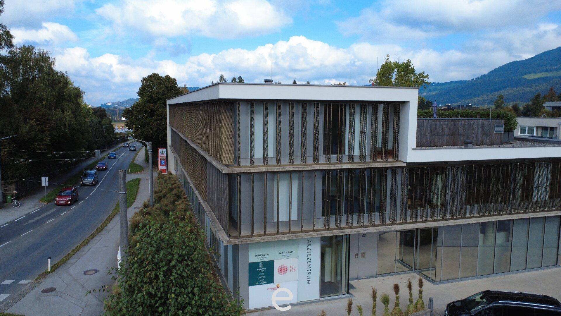 Ansicht des modernen Ärztezentrums mit seiner markanten Glasfassade und den vertikalen Lamellen unter blauem Himmel.