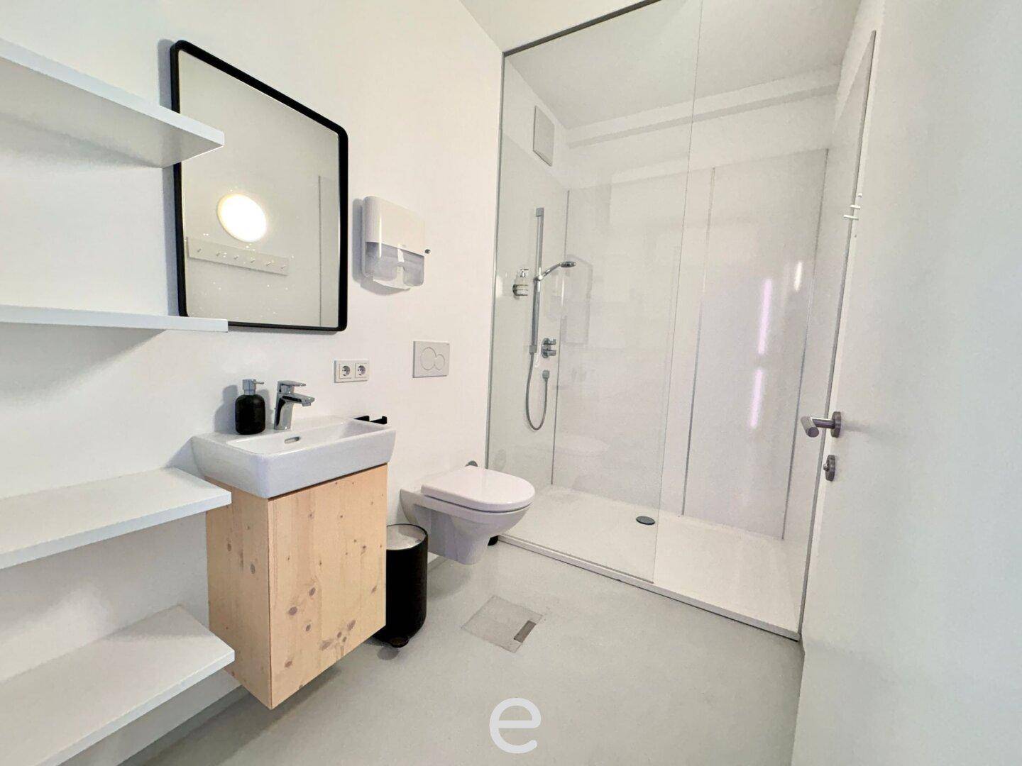 Modernes Badezimmer mit ebenerdiger Dusche, Waschbecken und WC, in hellen Farben gehalten.
