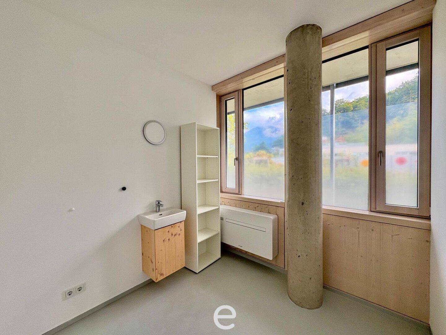 Helles Büro oder Behandlungszimmer mit Waschbecken, großem Fenster und einem Betonpfeiler.
