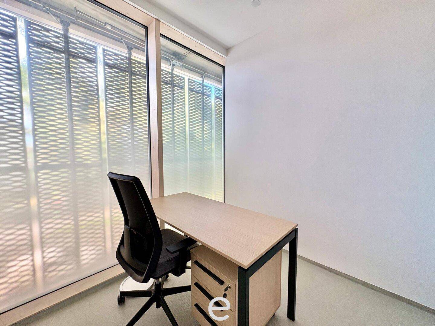 Modernes Büro mit Schreibtisch und Bürostuhl, ausgestattet mit großen Fenstern für optimale Beleuchtung.