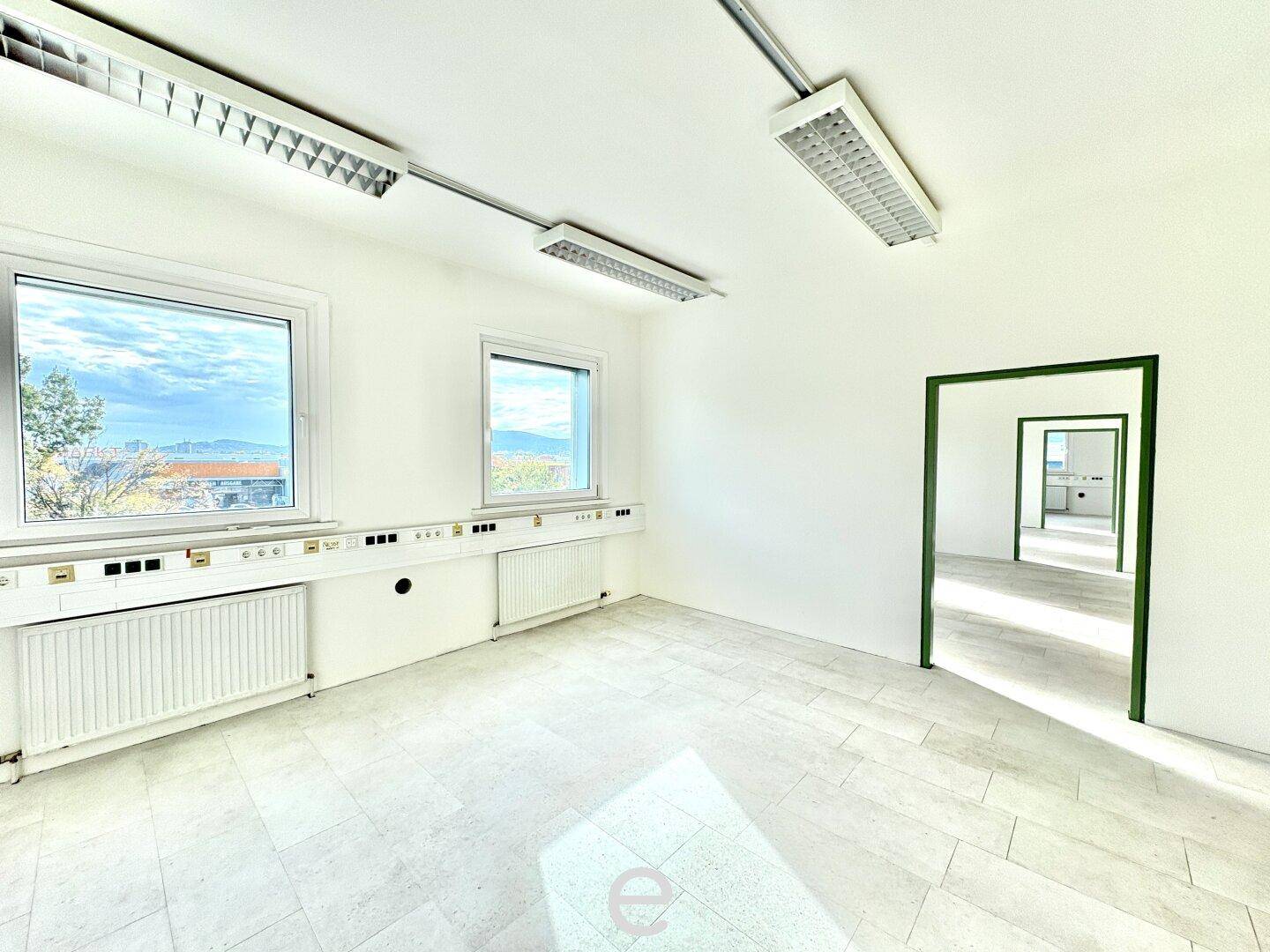 Helles Büro mit zwei Fenstern, Fliesenboden und grünen Türrahmen, ideal für Arbeitsbereiche.