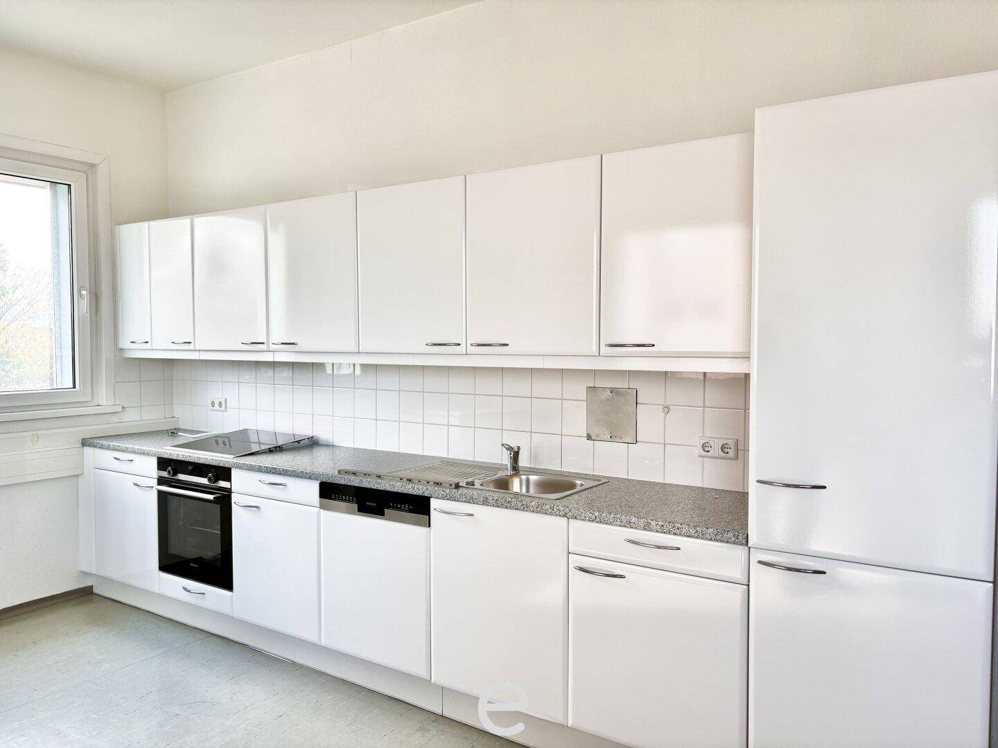 Moderne weiße Küche mit Einbaugeräten, grauer Arbeitsplatte und Fenster, ideal für den täglichen Gebrauch.