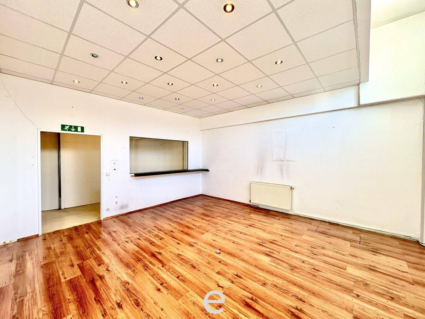 Kleinerer Büroraum mit Laminatboden, Rasterdecke und einer Durchreiche, ideal für Empfang oder Pausenbereich.