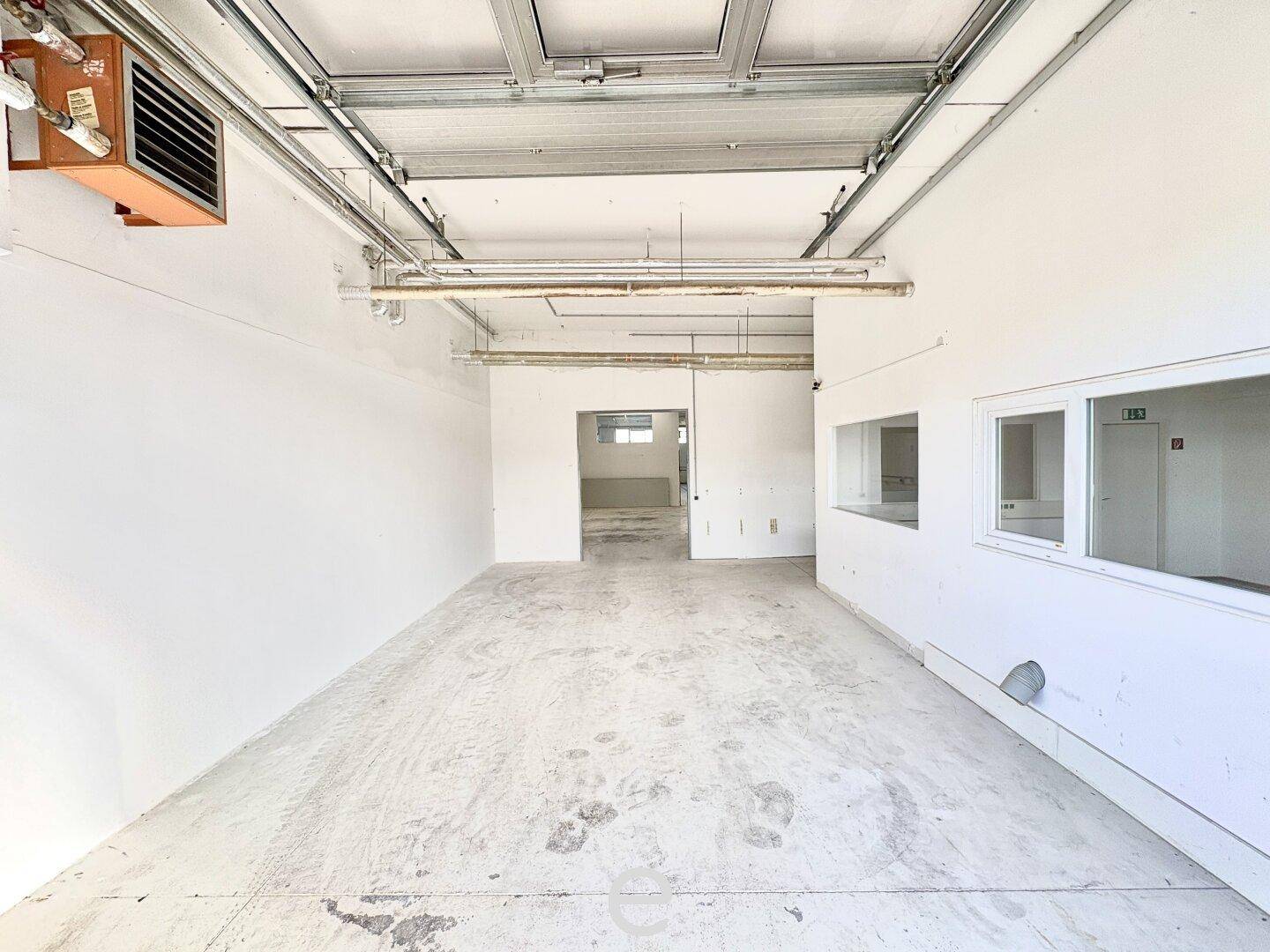 Geräumiger Lagerbereich mit hohen Decken, sichtbaren Installationen und einem Heizlüfter an der Wand.