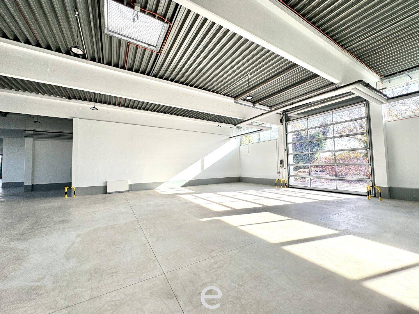 Heller Innenraum einer Industriehalle mit Betonboden, hohen Decken und einem großen Glas-Sektionaltor.