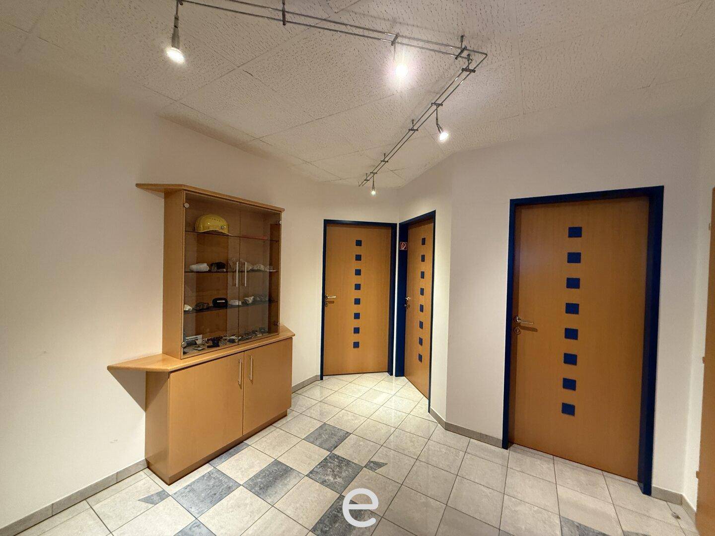 Flur mit karierten Fliesen, Holztüren und einer Vitrine für Ausstellungsstücke.