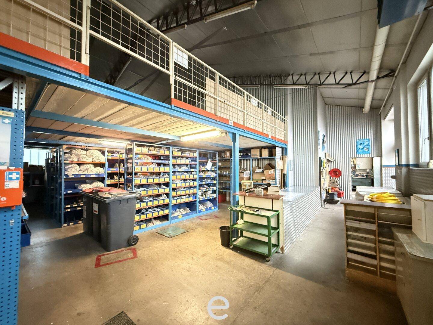 Lagerhalle mit Hochregalen, Arbeitsbereich und einer oberen Ebene für zusätzliche Lagerung.