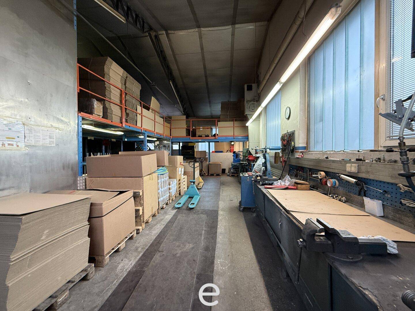 Lagerbereich mit Werkbank, Kartons und einem Hubwagen in einer industriellen Umgebung.