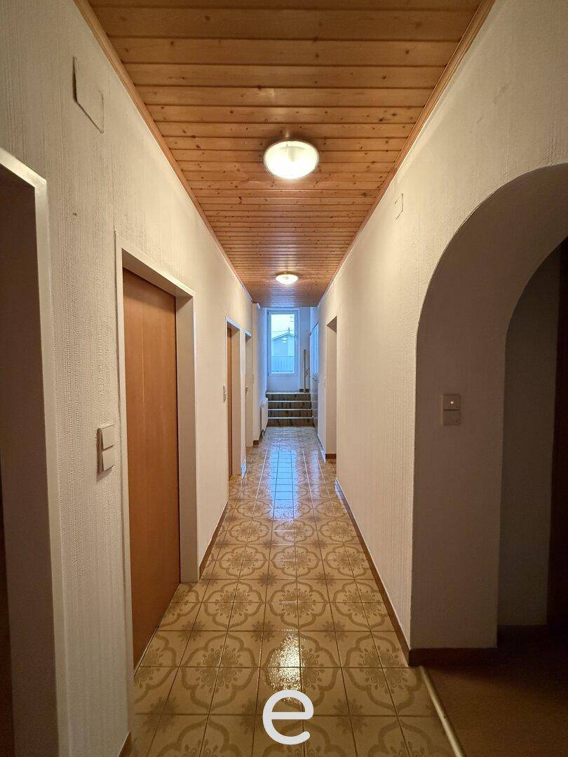 Langer Flur mit gemusterten Fliesen, Holzdecke und mehreren Türen zu den Räumen.