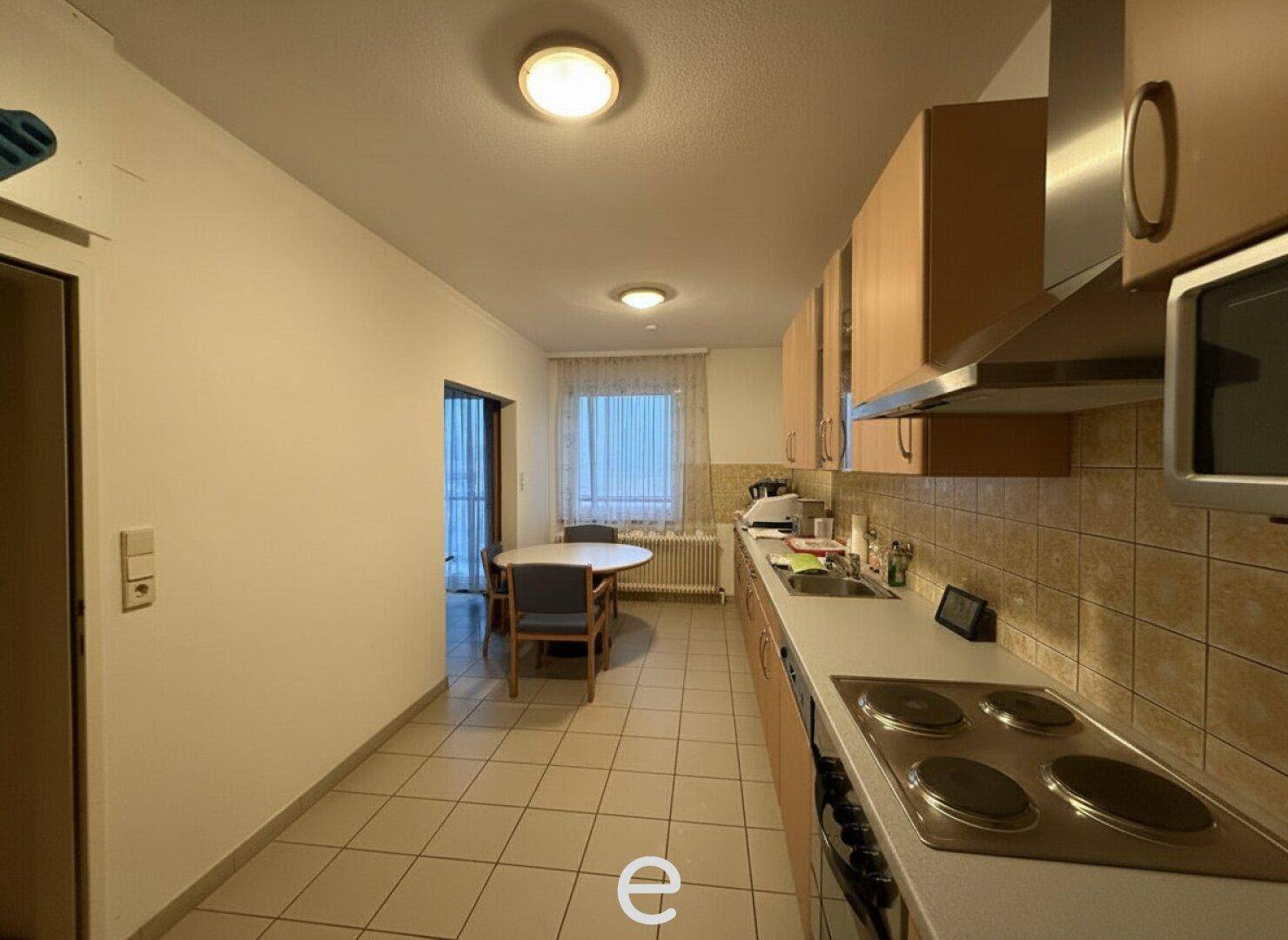 Funktionale Küche mit Fliesenboden, Einbauküche und kleinem Essbereich am Fenster.