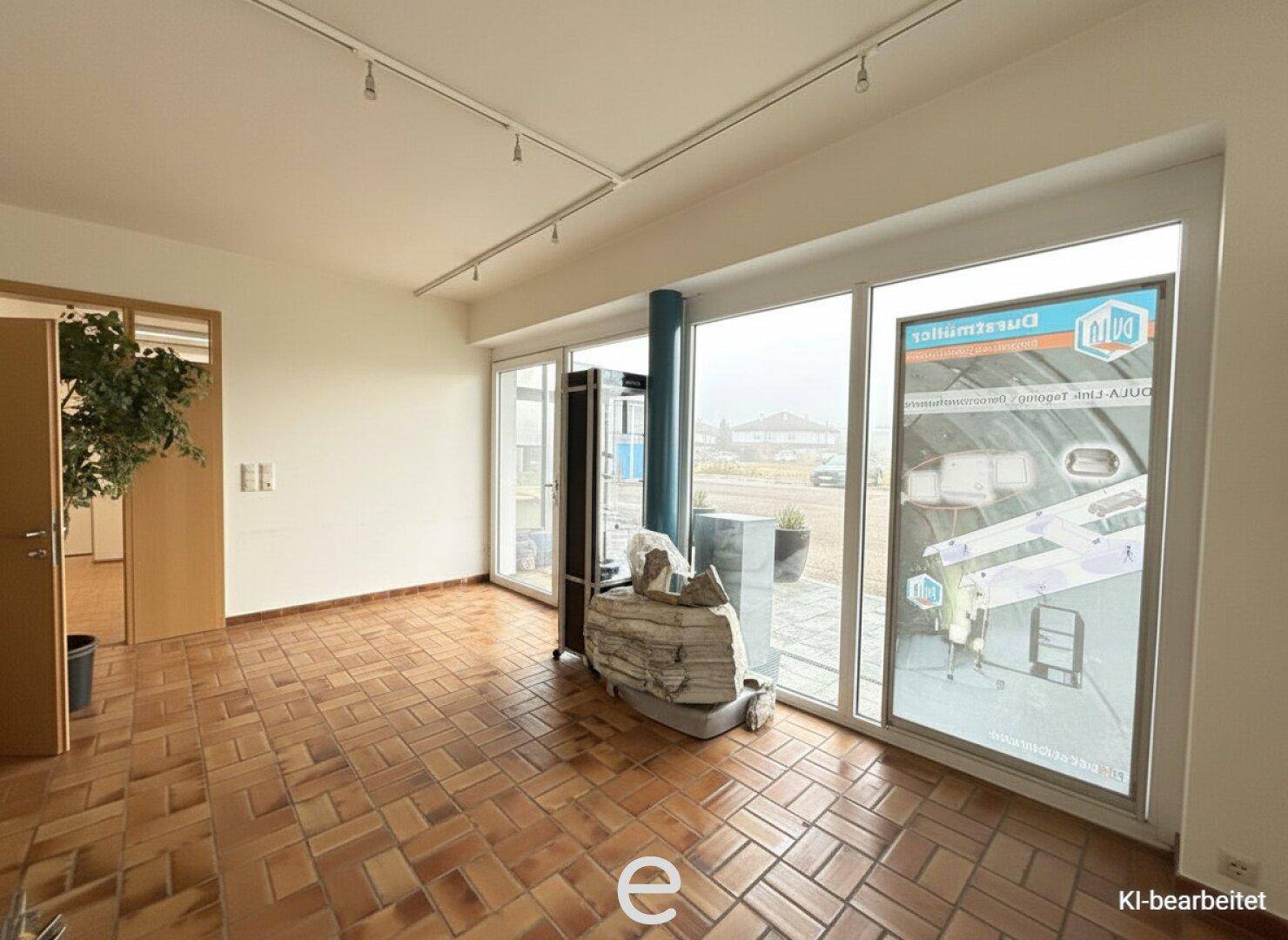 Geräumiger Ausstellungsraum mit Terrakottafliesen und großen Fensterfronten zur Straße.