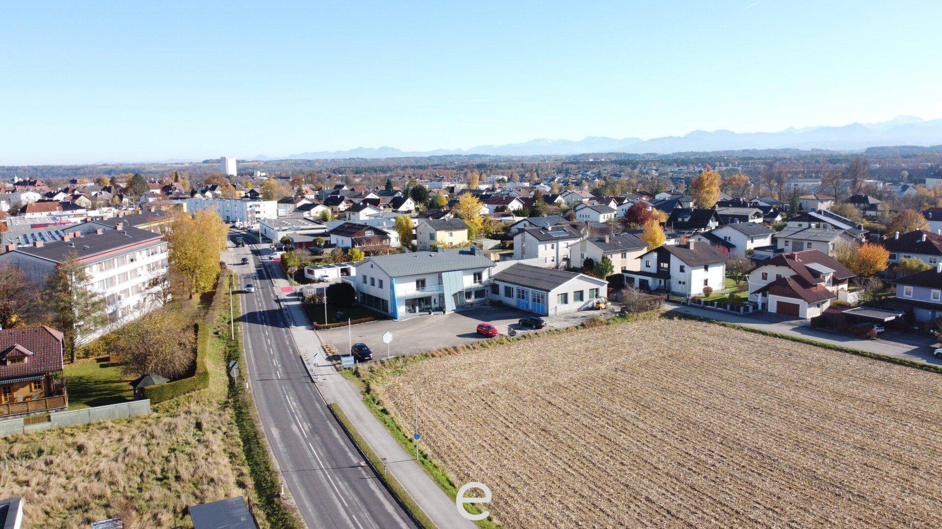 Weitläufige Luftaufnahme des Grundstücks mit umliegender Wohnbebauung und Alpenpanorama im Hintergrund.