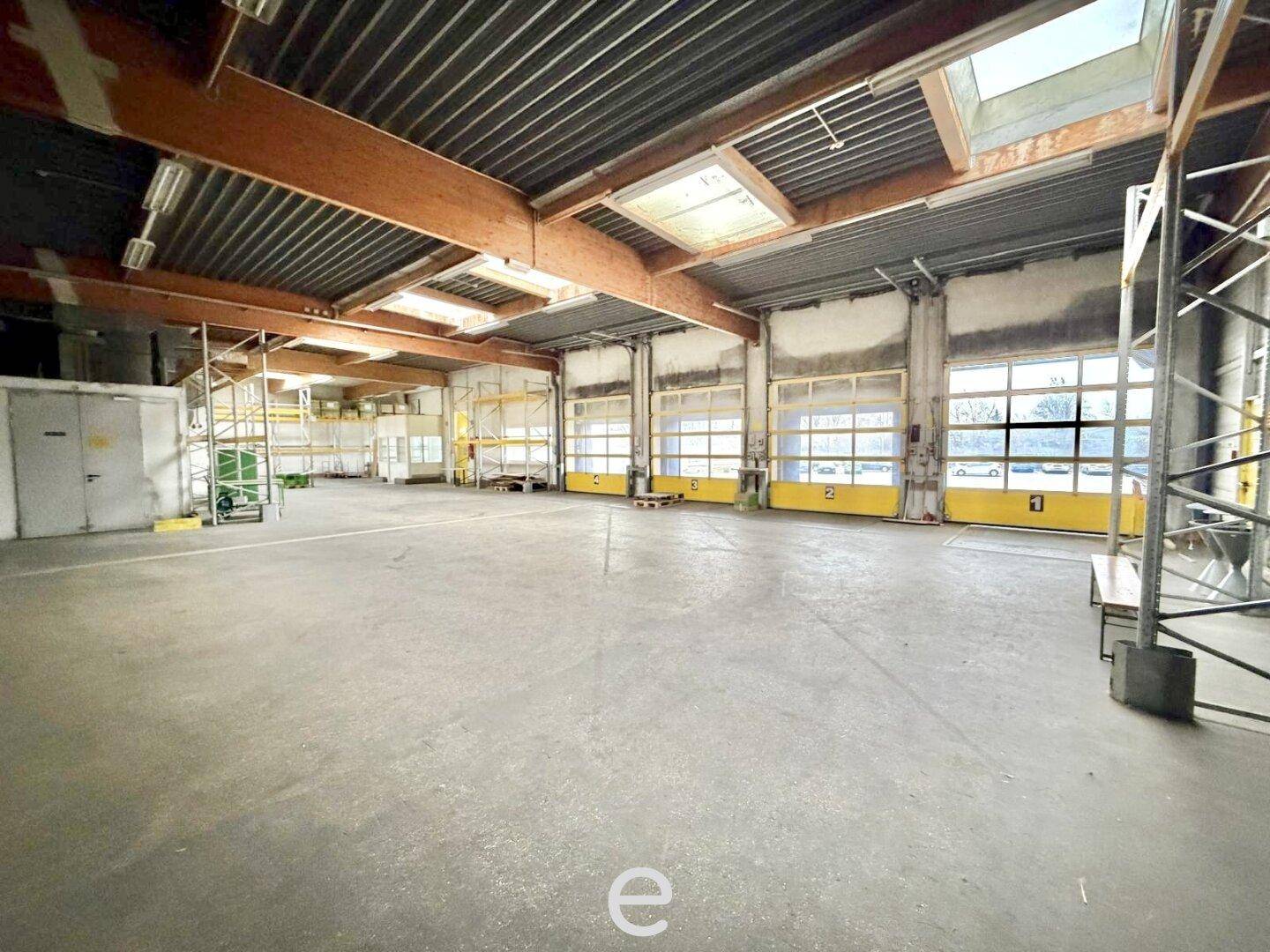 Innenansicht einer Lagerhalle mit Rolltoren und Oberlichtern, bietet direkten Zugang für Lieferungen.