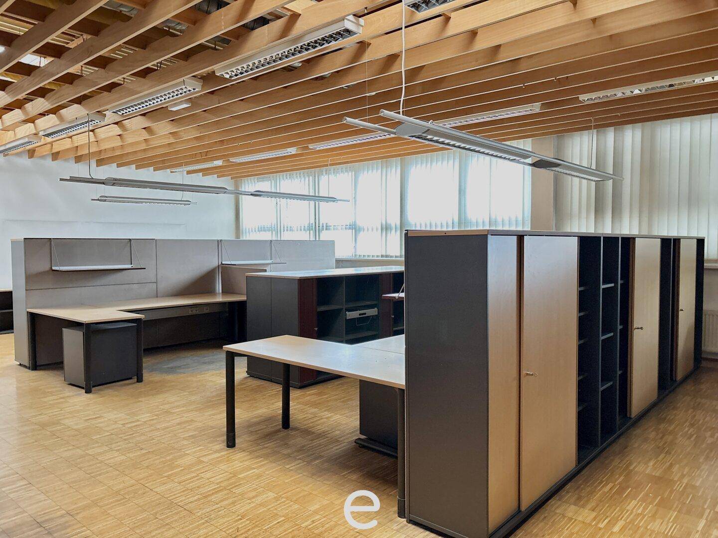 Großraumbüro mit Holzboden, modernen Möbeln und viel Tageslicht, ideal für produktives Arbeiten.