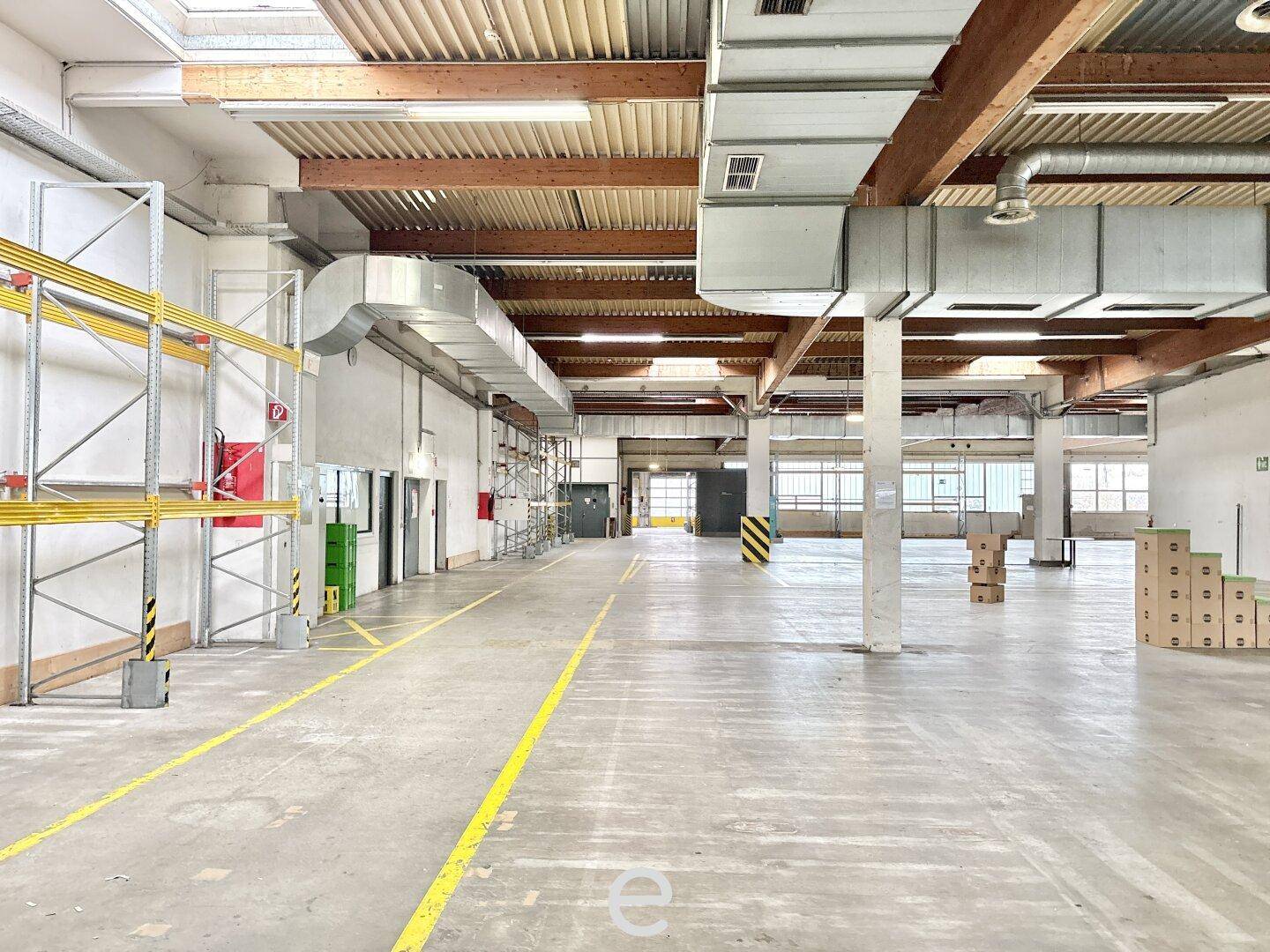 Weitläufige Lagerfläche mit Betonboden, Oberlichtern und sichtbaren Lüftungsrohren, bietet viel Stauraum.