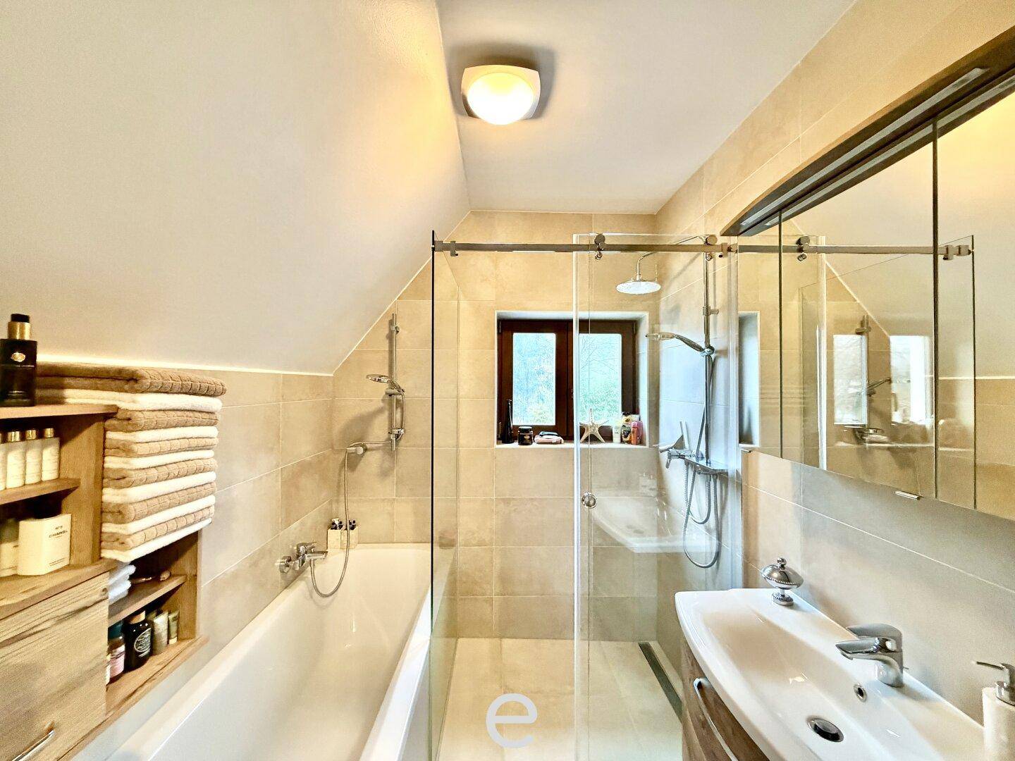 Badezimmer mit Badewanne, Dusche, Fenster und Dachschräge.