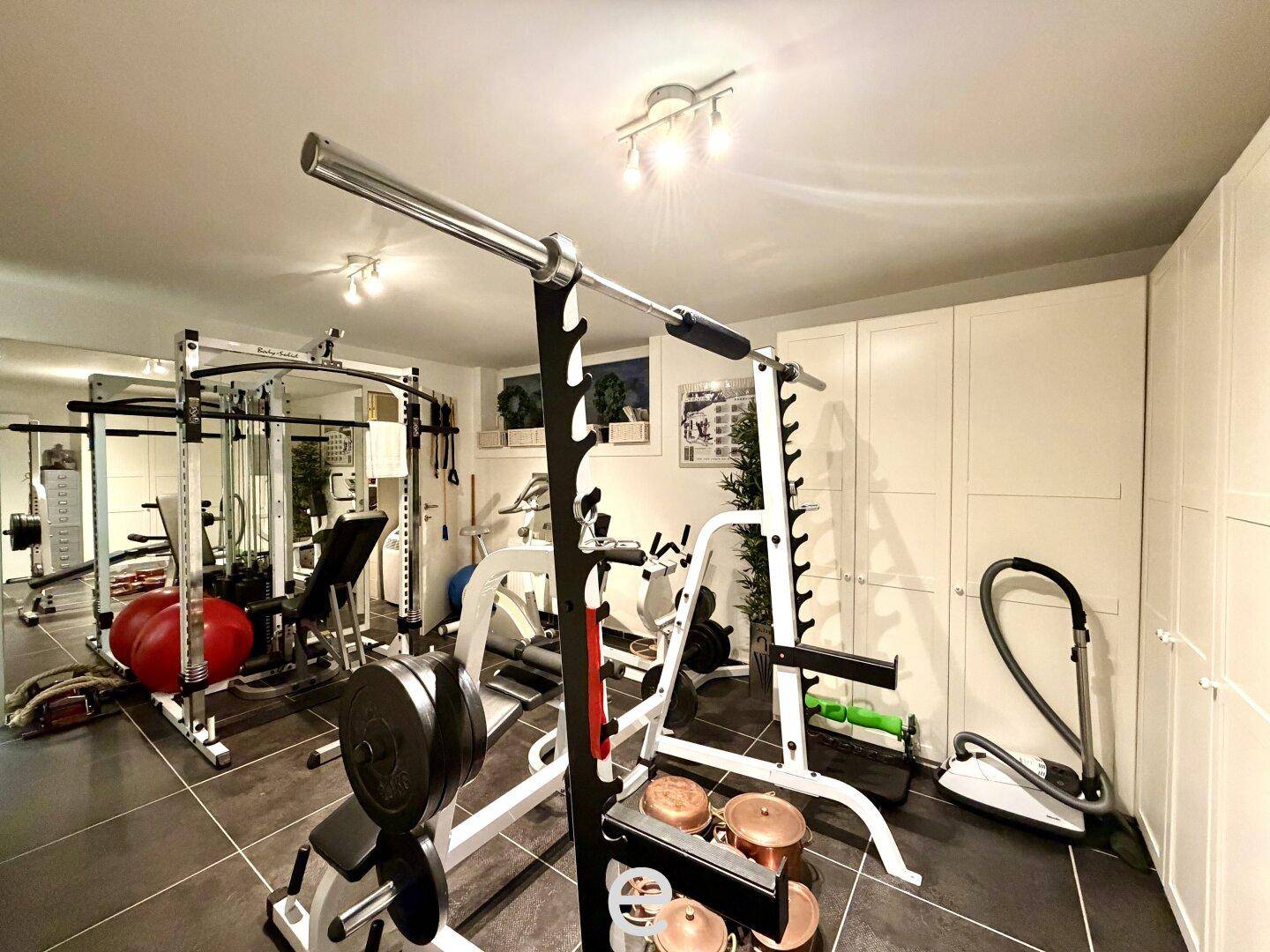 Privater Fitnessraum mit verschiedenen Trainingsgeräten und Spiegelfronten.