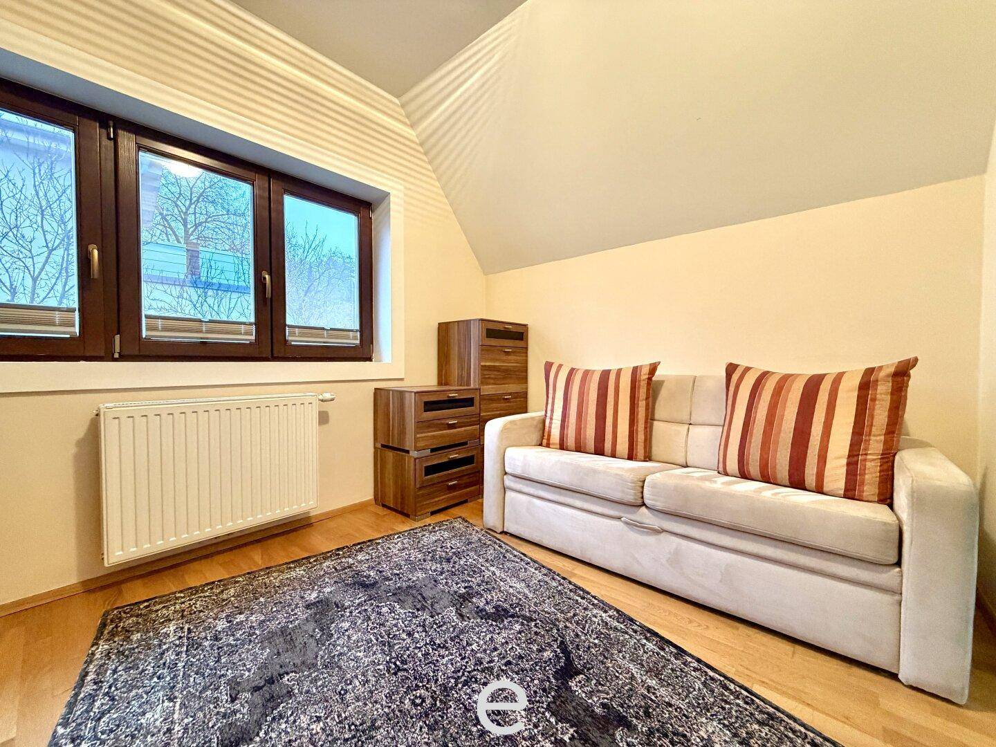 Helles Schlafzimmer mit Dachschräge, Schlafsofa und Holzmöbeln.