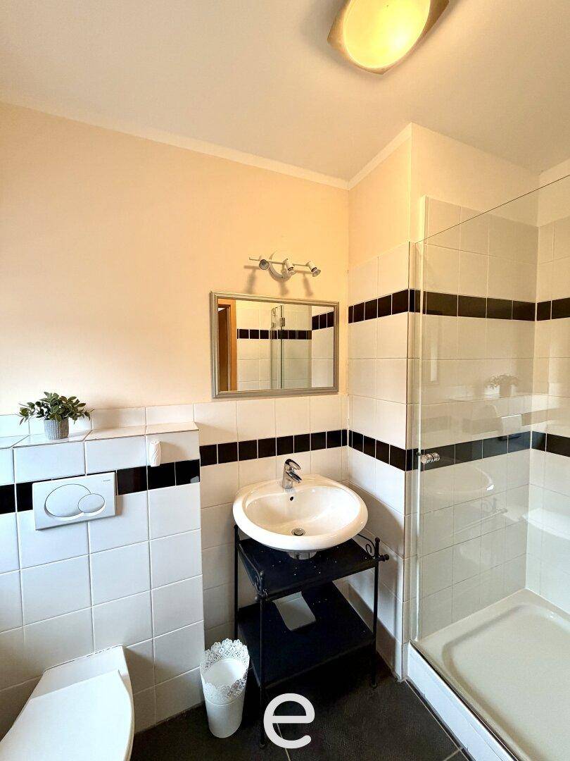 Badezimmer mit Dusche, WC und kontrastreichen schwarz-weißen Fliesen.