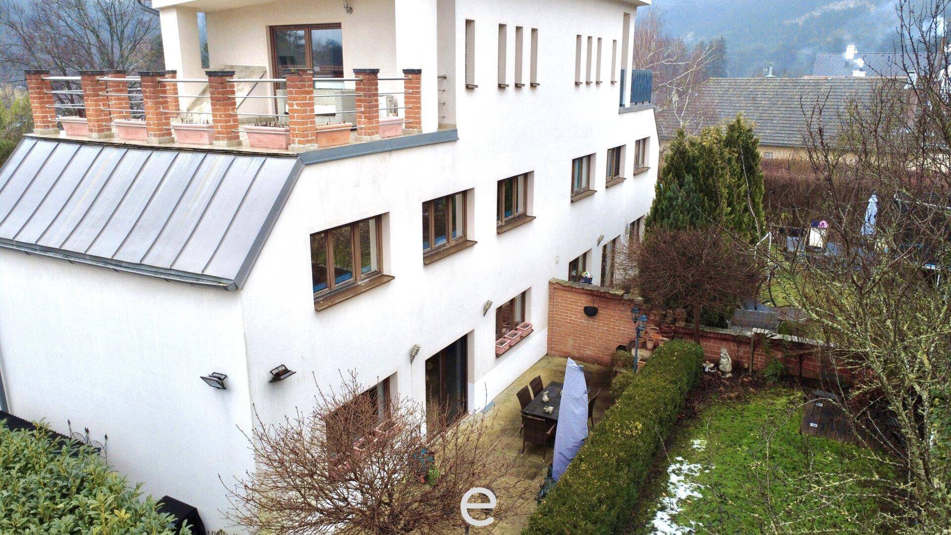 Außenansicht des Hauses mit weißer Fassade, Dachterrasse und Gartenbereich.