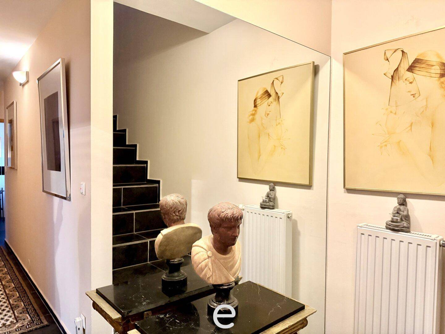 Heller Flur mit Treppe, Spiegel und dekorativen Büsten.