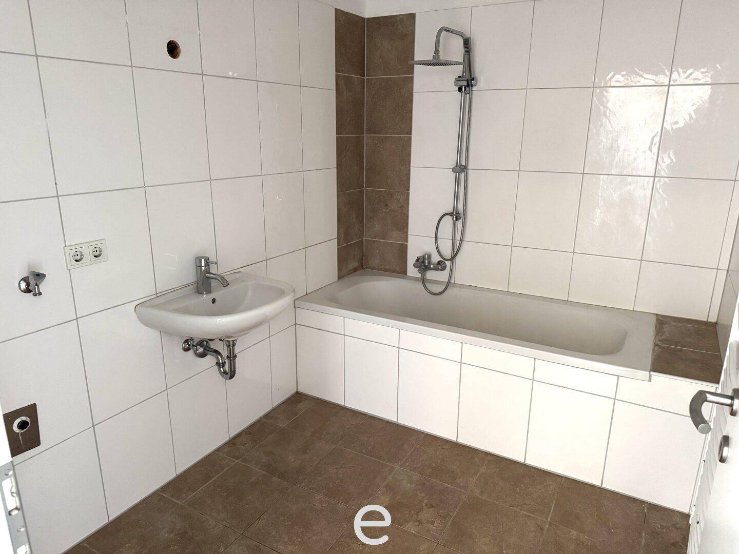 Gefliestes Badezimmer mit Badewanne, Duscharmatur und Waschbecken in neutralen Farben.
