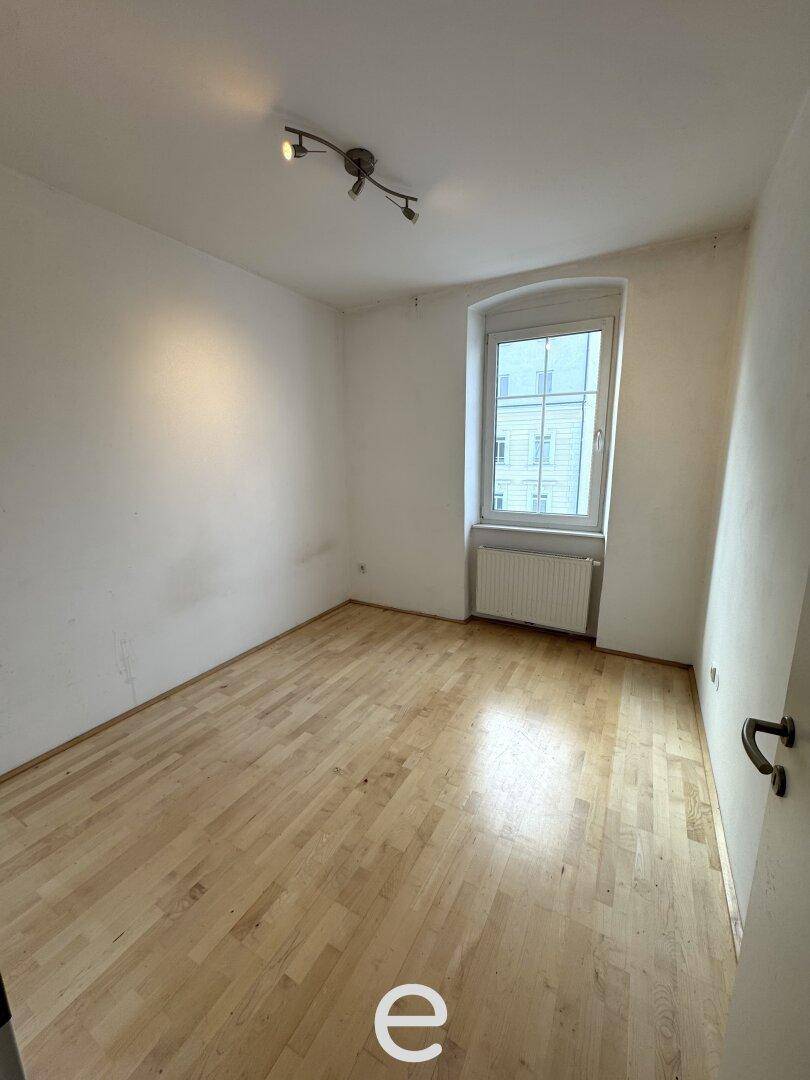 Schlafzimmer mit Holzboden, weiß gestrichenen Wänden und einem Fenster.