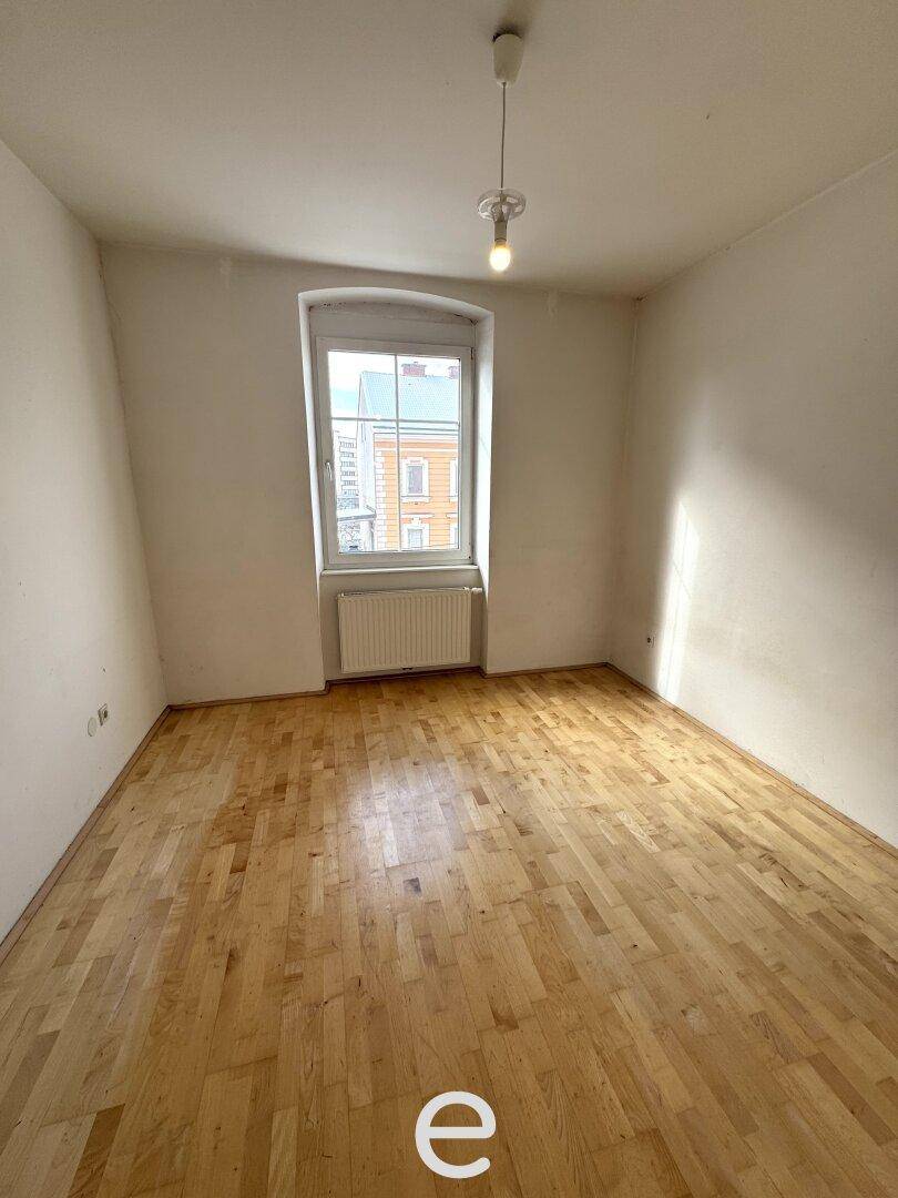 Helles Zimmer mit Holzboden und einem Fenster, das Tageslicht hereinlässt.