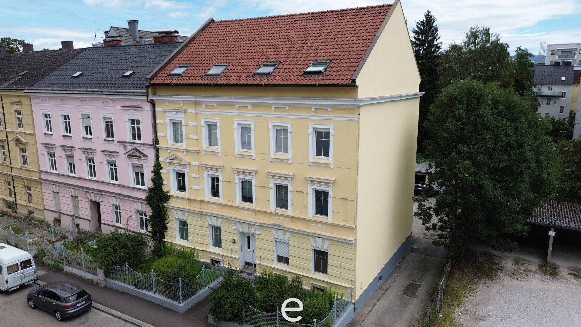 Historisches Mehrfamilienhaus mit gelber Fassade, roten Dachziegeln und Dachfenstern in städtischer Umgebung.