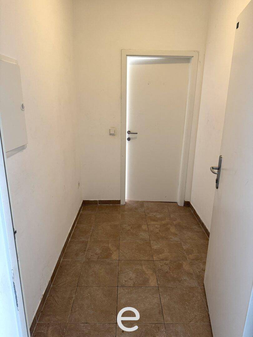 Flur mit braunen Fliesen, weißen Wänden und Zugang zu weiteren Räumen.