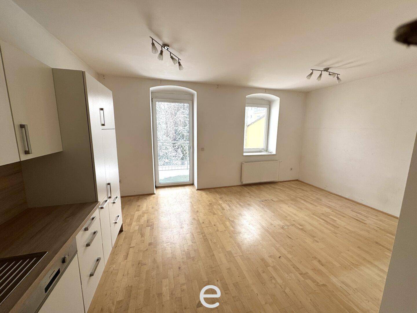 Heller Wohnbereich mit Holzboden, großen Fenstern und Zugang zu einem französischen Balkon.