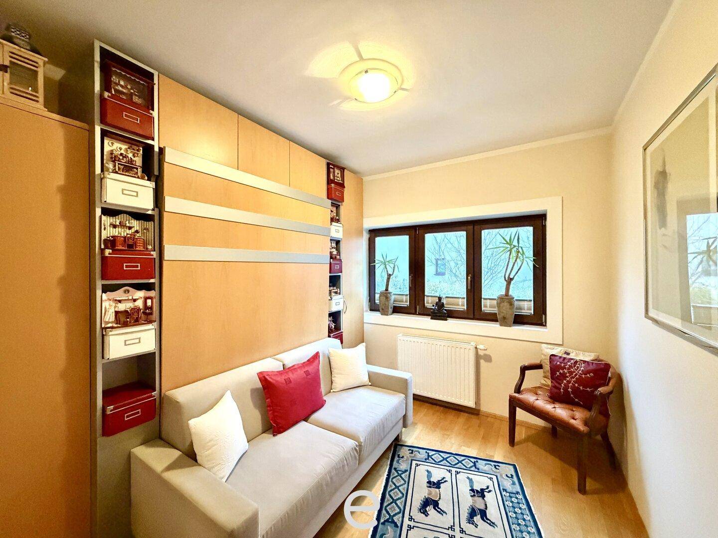 Helles Wohnzimmer mit beigem Sofa, integrierten Regalen und Blick ins Grüne durch das Fenster.