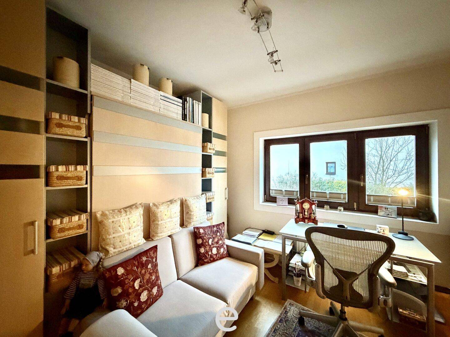 Funktionales Wohnzimmer mit Sofa, Schreibtisch und integrierten Regalsystemen für Stauraum.