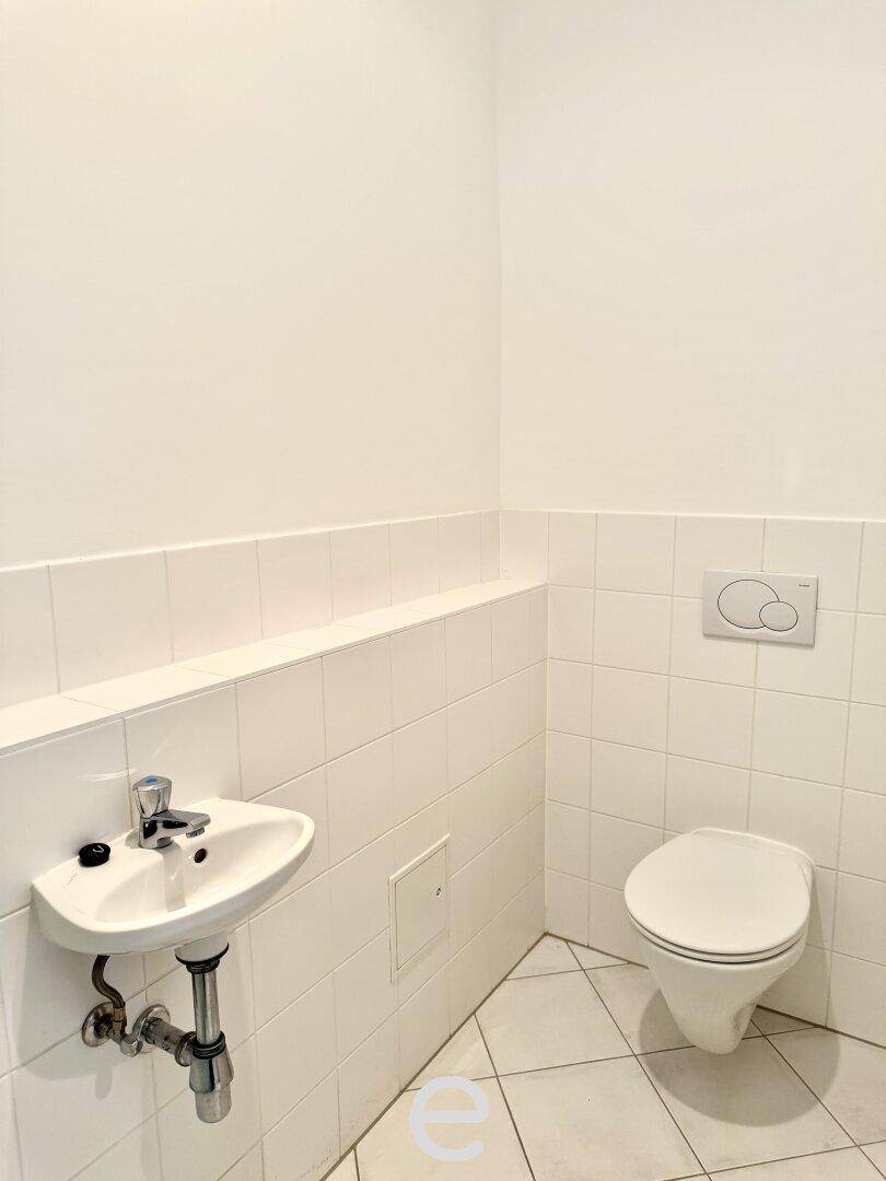 Kleines Gäste-WC mit wandhängender Toilette, kleinem Waschbecken und weißen Fliesen.