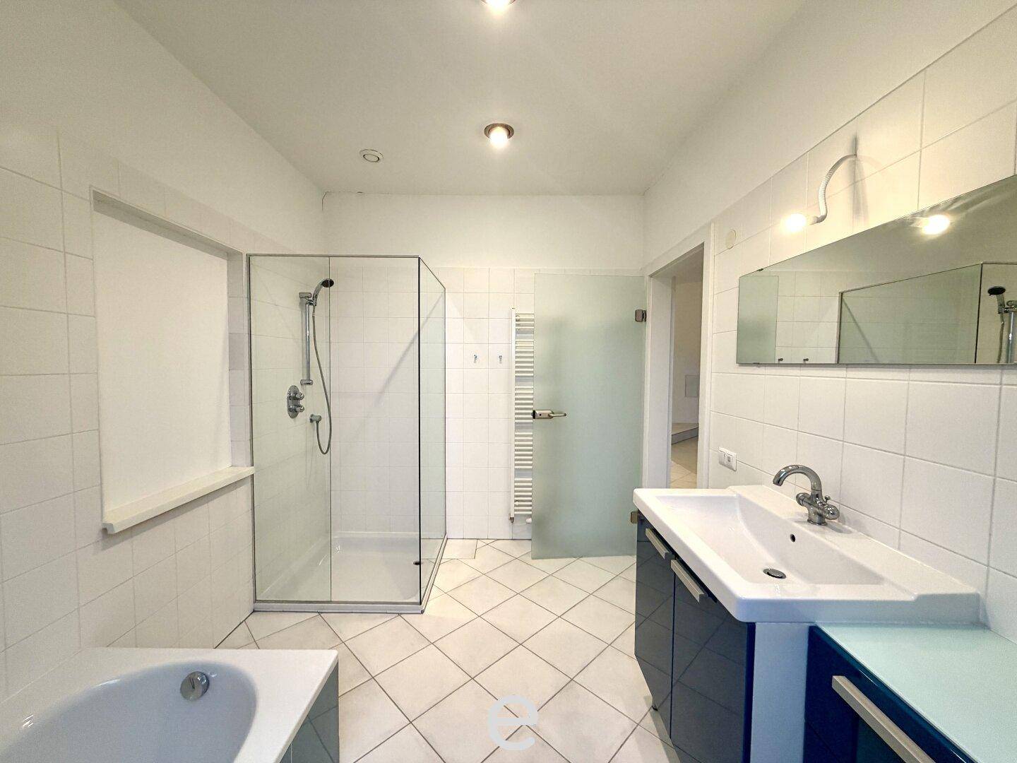 Geräumiges Badezimmer mit großer Duschkabine, Badewanne, modernem Waschtisch und Handtuchheizkörper.