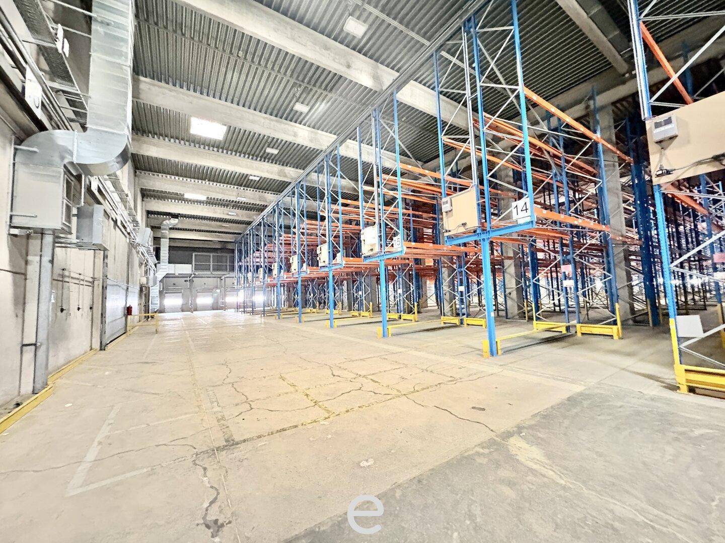 Industrieller Lagerraum mit hohen Decken, leeren Regalen und sichtbaren Lüftungsrohren, funktional und geräumig.
