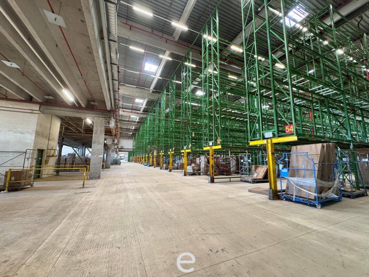 Weitläufige Lagerhalle mit hohen grünen Regalen und breiten Gängen, ideal für effiziente Logistikabläufe.