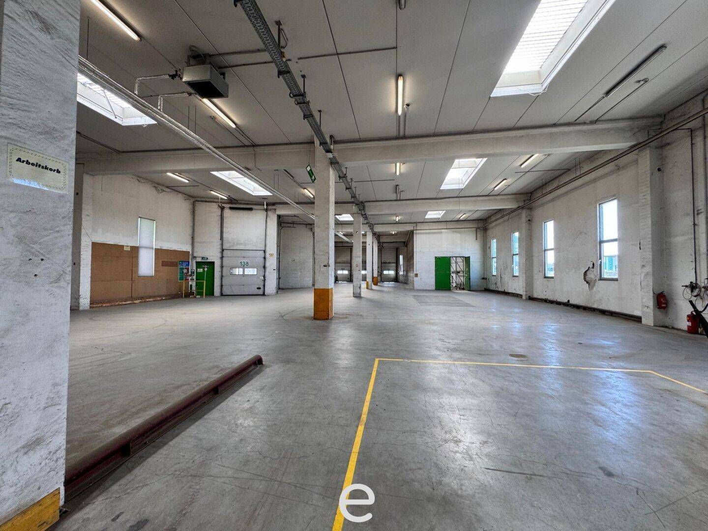 Geräumige Lagerhalle mit hohen Decken, Betonboden und mehreren Oberlichtern für natürliche Belichtung.