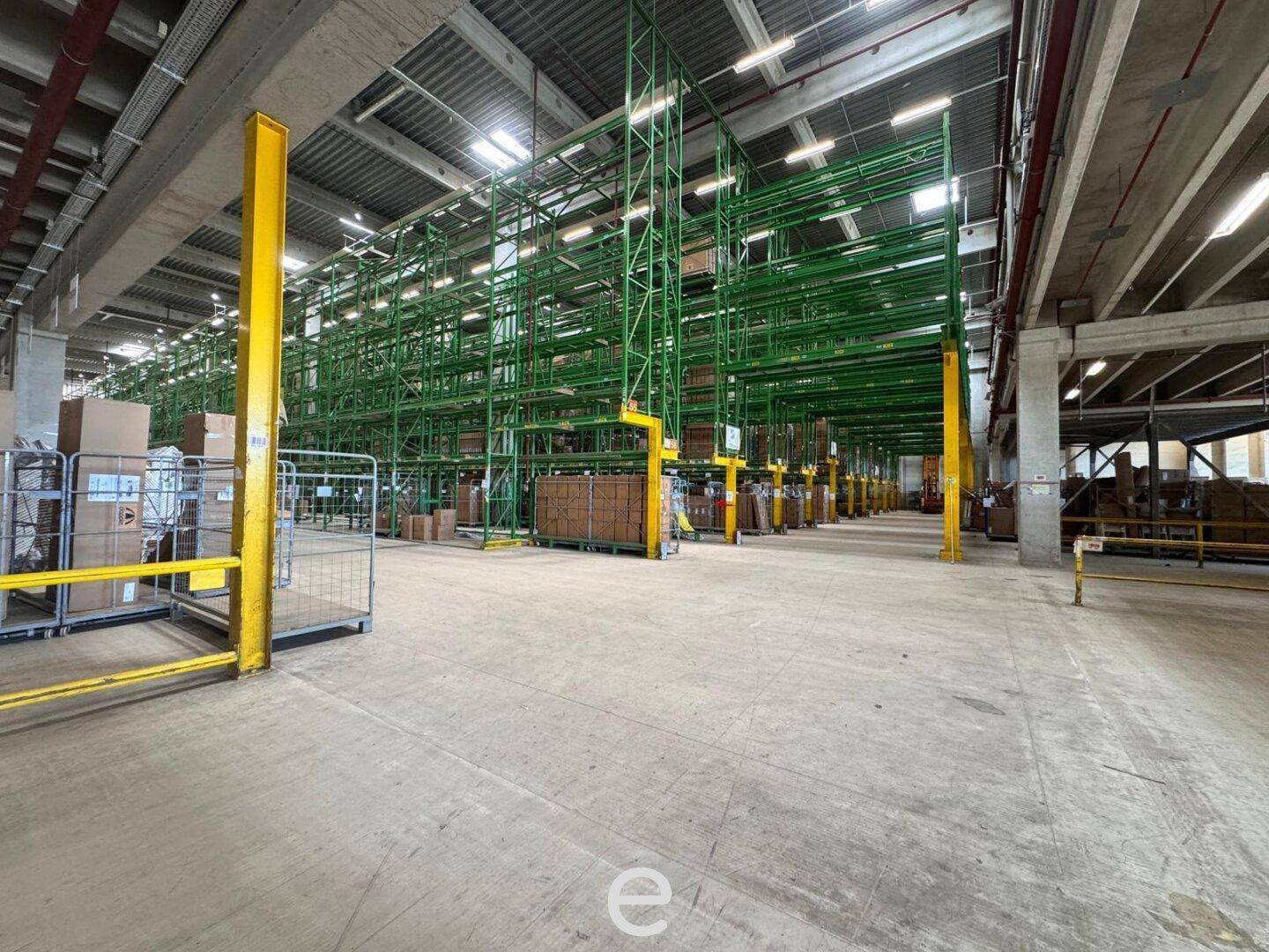 Geräumige Lagerhalle mit hohen grünen Regalsystemen und gelben Stützen, bereit für die Einlagerung von Waren.