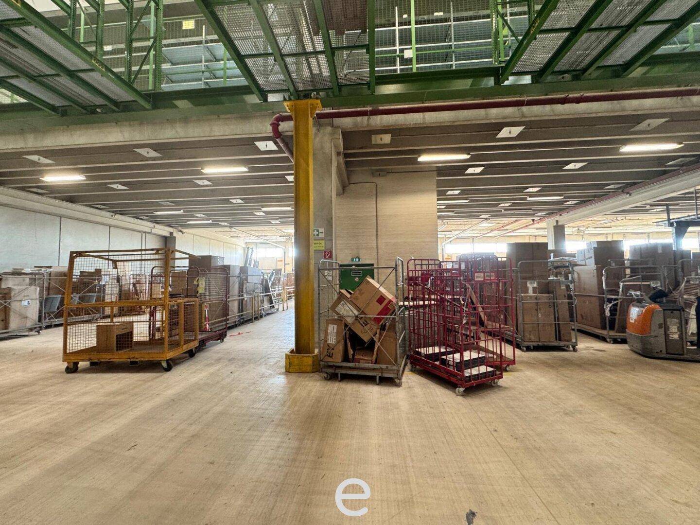 Lagerbereich mit verschiedenen Transportwagen und verpackten Waren auf dem Betonboden.