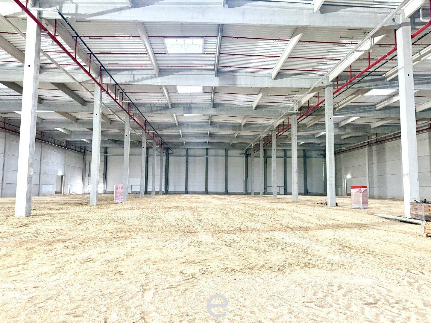 Ein weitläufiger Lagerraum mit vielen Betonpfeilern, hohen Decken und einem sandigen Boden, noch im Bau.
