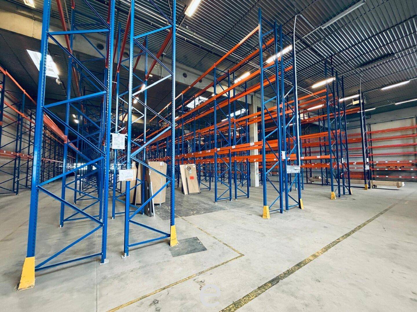 Weitläufige Lagerhalle mit hohen blauen und orangefarbenen Regalen und robustem Betonboden.