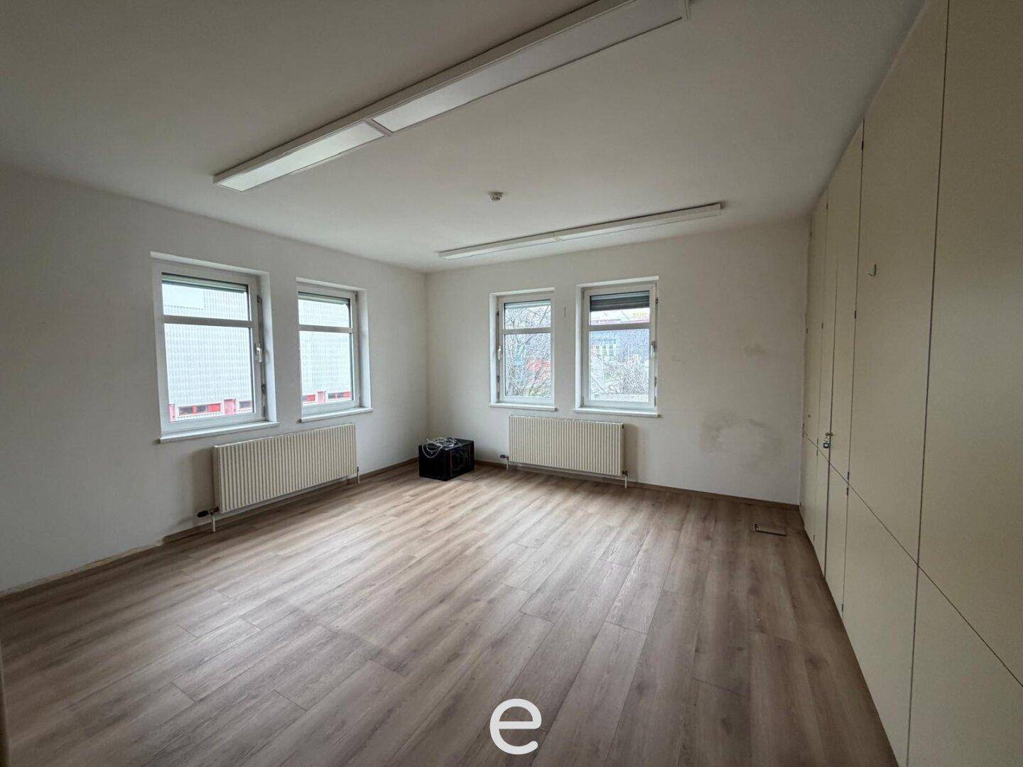 Helles Büro mit Laminatboden, Fenstern und integrierten Schränken, ideal für Büronutzung.