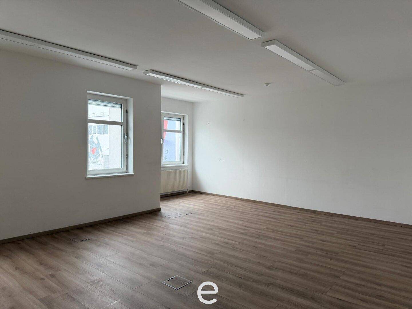 Geräumiges, helles Büro mit Laminatboden und mehreren Fenstern, ideal für flexible Arbeitsplatzgestaltung.