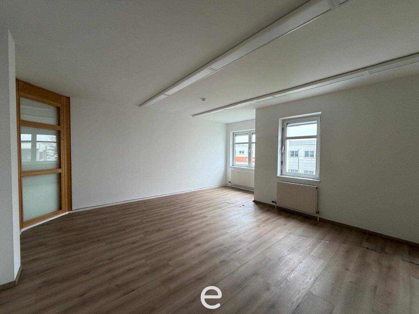 Helles, leeres Büro mit Laminatboden und Fenstern, bietet eine angenehme Arbeitsumgebung.
