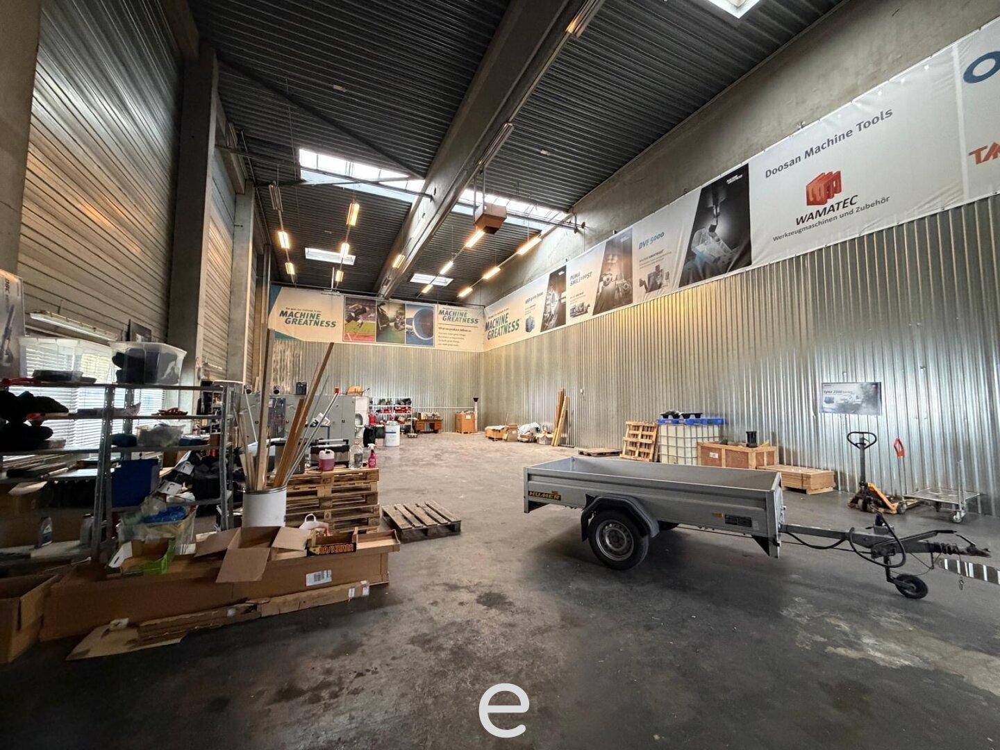 Großer Werkstattbereich mit hohen Decken, Betonboden und verschiedenen Arbeitsmaterialien.