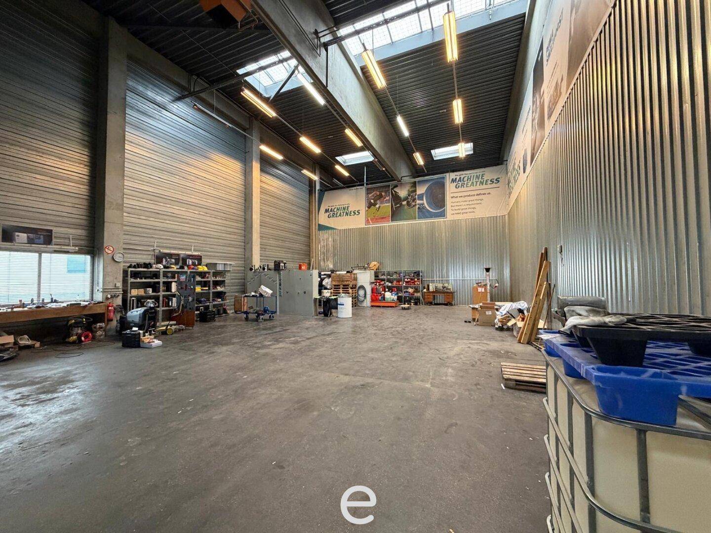 Geräumiger Werkstattbereich mit hohen Decken, Betonboden und verschiedenen Geräten und Materialien.