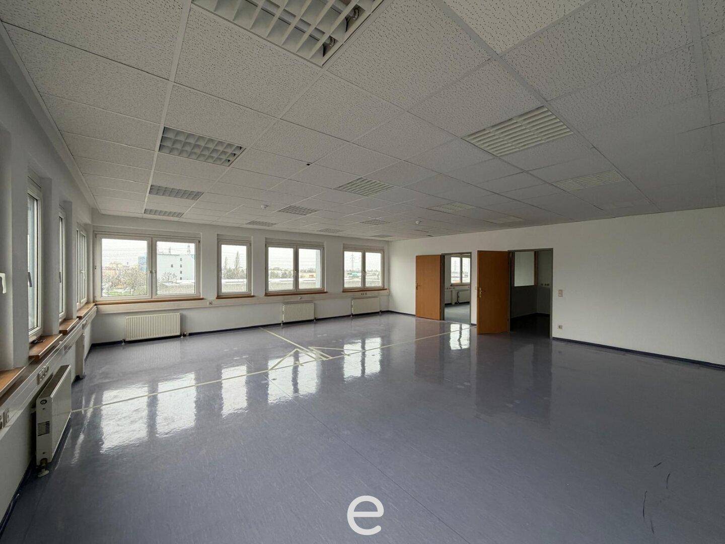 Großes, offenes Büro mit vielen Fenstern, Linoleumboden und abgehängter Decke, ideal für Großraumbüros.